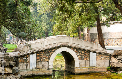Ancient stone bridge surrounded by ancient trees in the Imperial Summer Palace park. Beijing, China