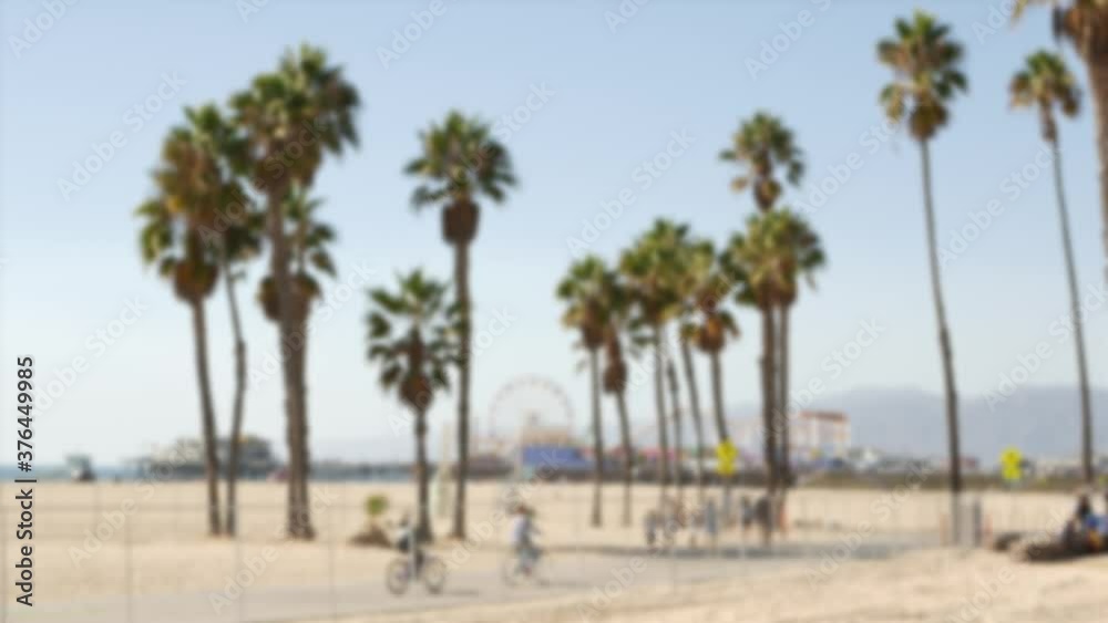 California beach aesthetic, people ride cycles on a bicycle path. Blurred, defocused background. Amusement park on pier and palms in Santa Monica american pacific ocean resort, Los Angeles CA USA. California beach aesthetic, people ride cycles on a bicycle path. Blurred, defocused background. Amusement park on pier and palms in Santa Monica american pacific ocean resort, Los Angeles CA USA.