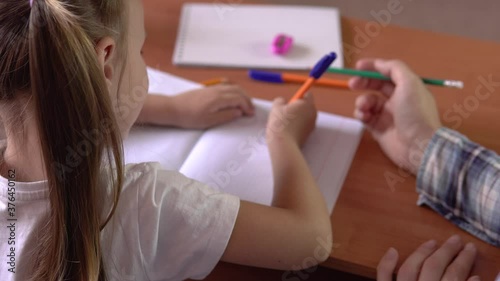 Preschool learning.A little girl with a teacher sits at a school desk and draws in a notebook with a pen.Drawing.4k