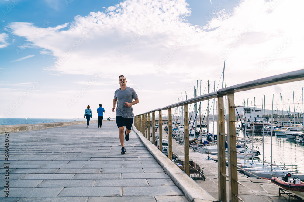 Smiling caucasian male jogger enjoying training on coastline feeling energy and vitality for keeping perfect body shape, 20s cheerful young man running on street on morning cardio workout Smiling caucasian male jogger enjoying training on coastline feeling energy and vitality for keeping perfect body shape, 20s cheerful young man running on street on morning cardio workout