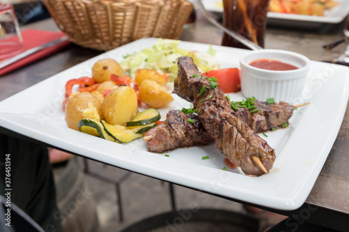Grilled meat skewers served with baked potatoes and hot chili sauce served as a traditional dish of French cuisine in the restaurant of Carcassonne, France