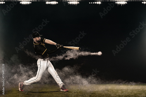 Baseball player with bat taking a swing on grand arena. Ballplayer on dark background in action. photo