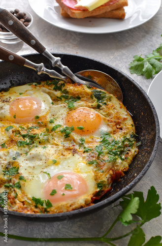 fried eggs with tomatoes, onions and parsley in a pan. Tasty breakfast. Light background. Shakshuka.