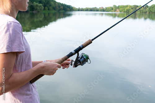 Cute woman is fishing with rod on the summer lake. Woman fishes on the river