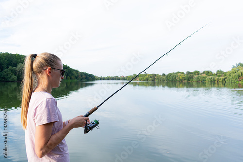 Cute woman is fishing with rod on the summer lake. Woman fishes on the river