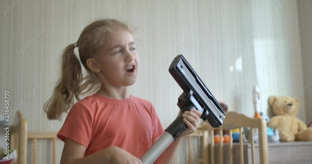 Little Fun Creative Girl Singing and Using Мacuum Сleaner Handle as Microphone. Child Using Mop as Guitar While Singing in Play Room. Enjoying Spring Cleaning. Playful Creative Kid Dancing With Mop. Little Fun Creative Girl Singing and Using Мacuum Сleaner Handle as Microphone. Child Using Mop as Guitar While Singing in Play Room. Enjoying Spring Cleaning. Playful Creative Kid Dancing With Mop.