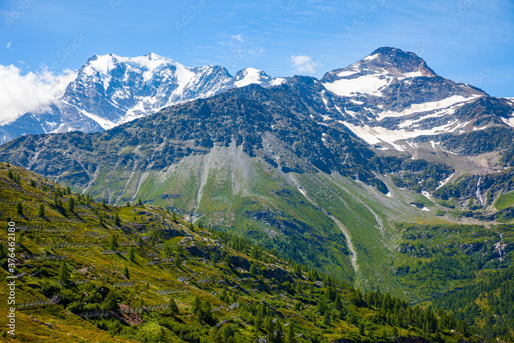Unique summer Alpine landscape seen from Simplon Pass with rocky mountain ranges and greenery on foothills in Switzerland.