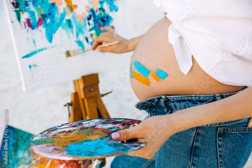 Closeup of a pregnant woman artist painting with a paintbrush, holding a palette.