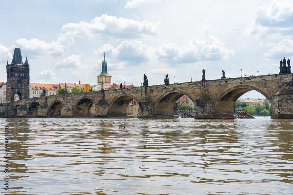 old stone tower on Charles Bridge from 1402 and old architecture and blue sky in the background in the center of Prague in the Czech Republic next to the Vltava River