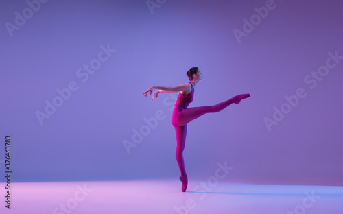 Dynamic. Young and graceful ballet dancer isolated on purple studio background in neon light. Art, motion, action, flexibility, inspiration concept. Flexible caucasian ballet dancer, weightless jumps.