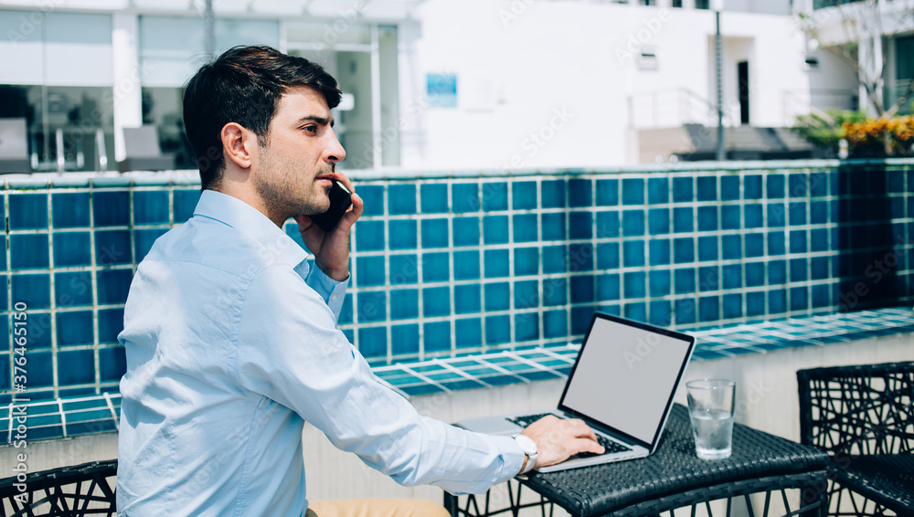 Focused young businessman speaking on phone working on terrace Focused young businessman speaking on phone working on terrace