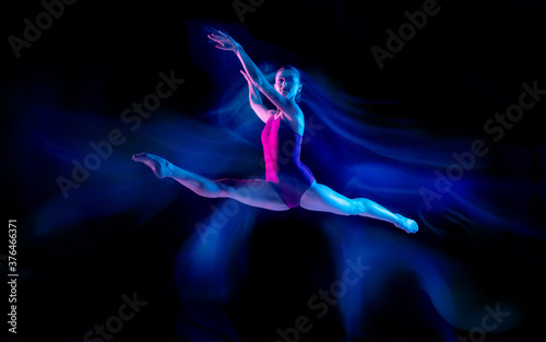 Ghost. Young and graceful ballet dancer on black studio background in neon mixed light. Art, motion, action, flexibility, inspiration concept. Flexible caucasian ballet dancer, weightless jumps.