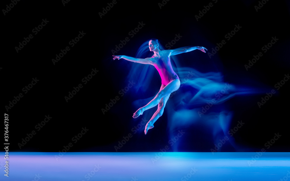 Ghost. Young and graceful ballet dancer on black studio background in neon mixed light. Art, motion, action, flexibility, inspiration concept. Flexible caucasian ballet dancer, weightless jumps.