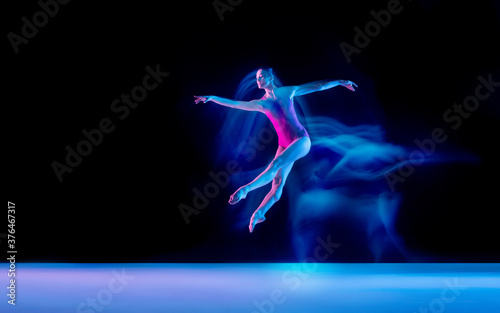 Ghost. Young and graceful ballet dancer on black studio background in neon mixed light. Art, motion, action, flexibility, inspiration concept. Flexible caucasian ballet dancer, weightless jumps. © master1305