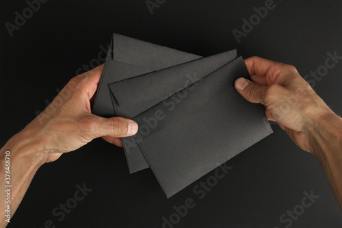 two hands holds three blank black envelopes on black background, mockup, copy space