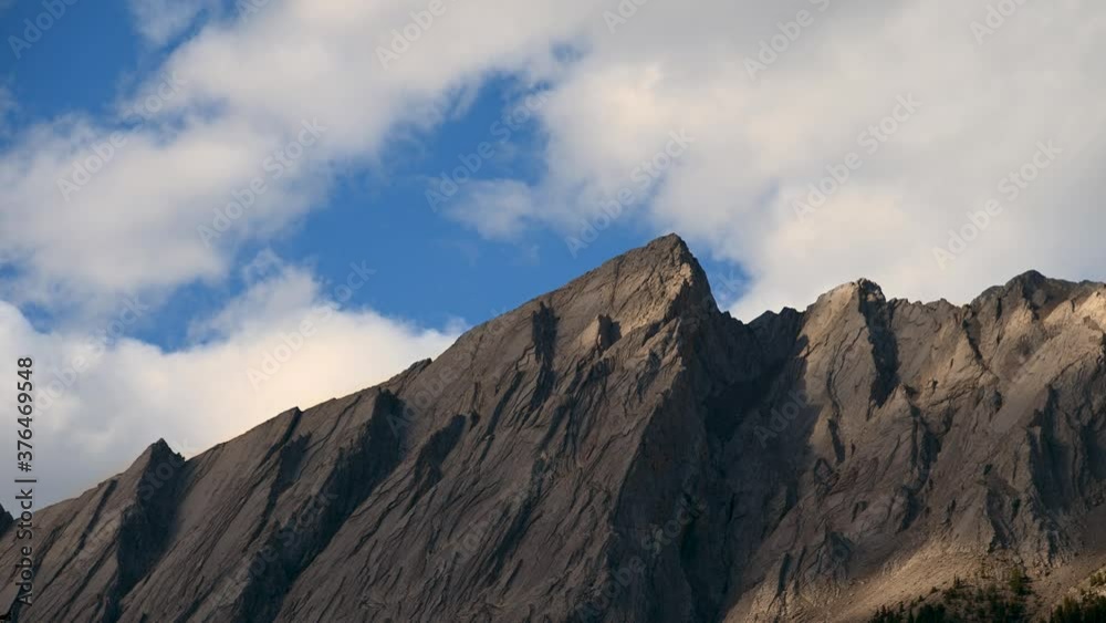 Dramatic clouds move through a blue sky above a large grey to brown mountain cliff in this time lapse.
Dramatic clouds move through a blue sky above a large grey to brown mountain cliff in this time lapse.