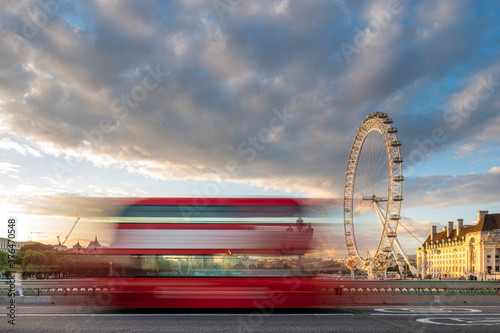A red London bus goes past in a blur across Westminster Bridge with the London Eye and Southbank in distance, London, England