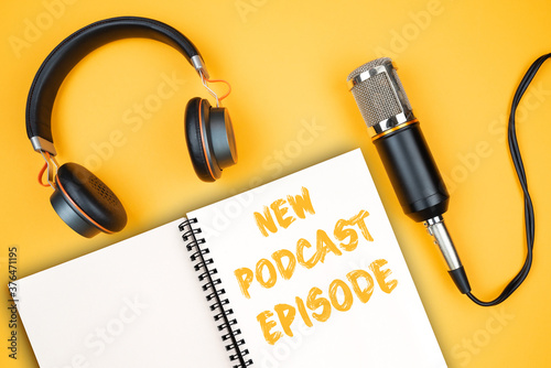 NEW PODCAST EPISODE text on notepad next to headphones and recording microphone, podcasting concept on orange background photo