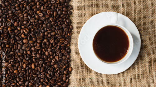 top view of cup of coffee on saucer with coffee beans and sackcloth on background