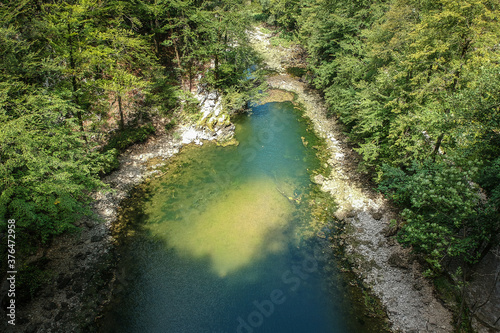 A round small lake called Divje jezero in Slovenia, surrounded with pebbles and still water on a sunny day with blue skies, hiding between thick green forest. photo