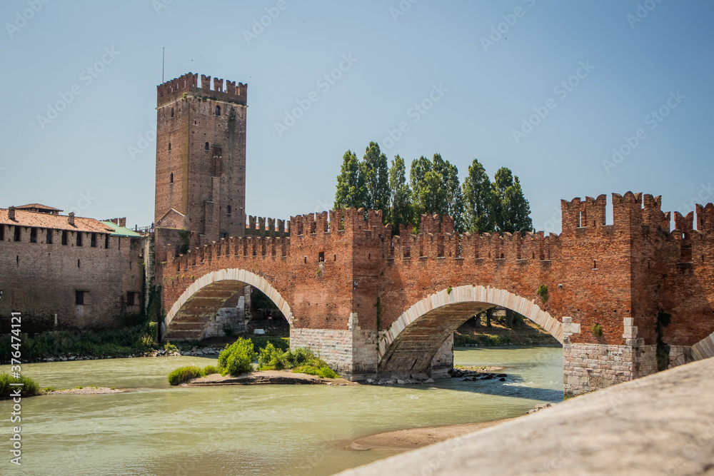 Castel vecchio bridge in Verona, Italy on a sunny day. Beautiful brick wall above the river of Adige on a blue sky with visible tower of the castle.