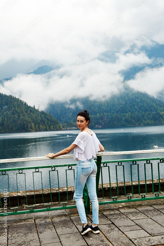 A girl in white clothing on a background of a mountain lake with blue water and mountains with clouds. Background.