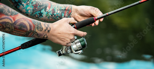 Fishing background - Close up of tattooed man holding a fishing rod in his hands and fishing at the lake