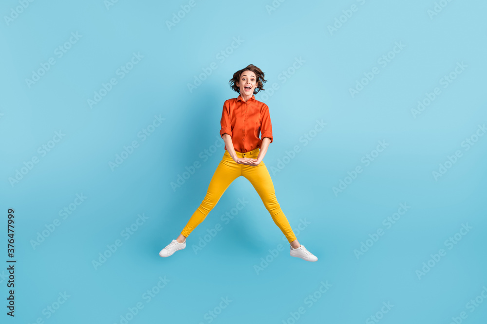 Full size photo of pretty crazy funky lady jump high up good mood spend summer holidays vacation free time wear orange shirt yellow trousers sneakers isolated blue color background Full size photo of pretty crazy funky lady jump high up good mood spend summer holidays vacation free time wear orange shirt yellow trousers sneakers isolated blue color background