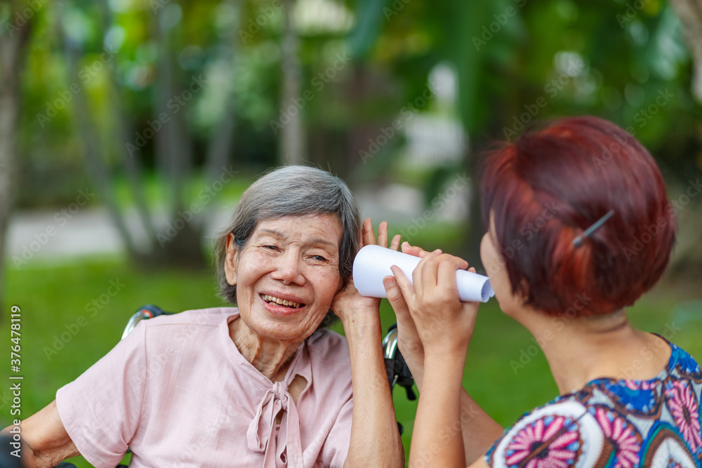 Daughter talking to hearing impaired elderly woman , using paper tube Daughter talking to hearing impaired elderly woman , using paper tube
