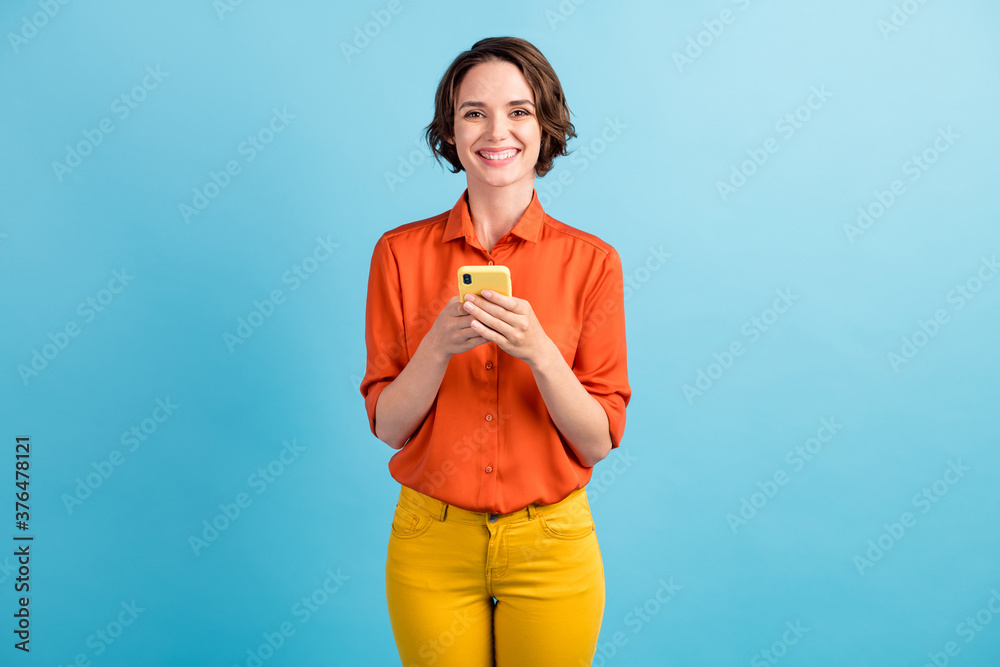 Photo of pretty lady blogger freelancer good mood chatting telephone writing post comments check likes reposts shares wear orange shirt yellow trousers isolated blue color background Photo of pretty lady blogger freelancer good mood chatting telephone writing post comments check likes reposts shares wear orange shirt yellow trousers isolated blue color background