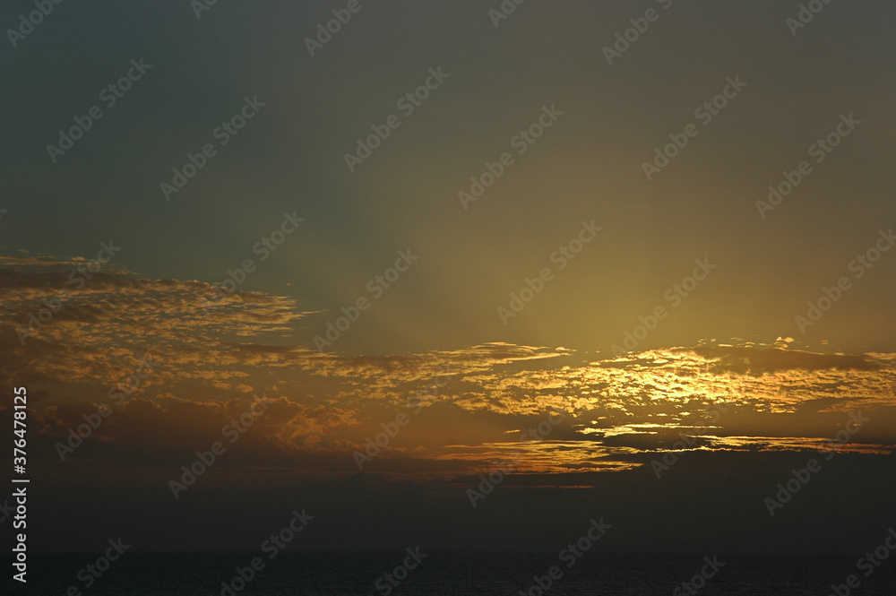 Dramatic sunset with beautiful and faint rays of light through the golden clouds, Tenerife, Canary Islands, Spain, ethereal sky with a dark and heavy horizon, thin sunrays and thin clouds in soft hues