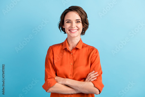 Photo of attractive bossy lady bobbed hairdo arms crossed self-confident person worker friendly smile white teeth good mood wear orange office shirt isolated blue color background