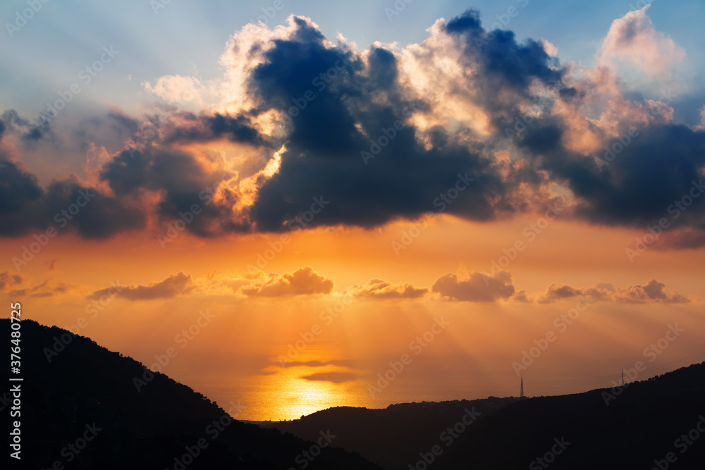 Stunning sunset over the Mediterranean Sea in Lebanon. Bright orange and blue sky and clouds. Silhouettes of mountains in the rays of the sun. Incredible wallpaper
