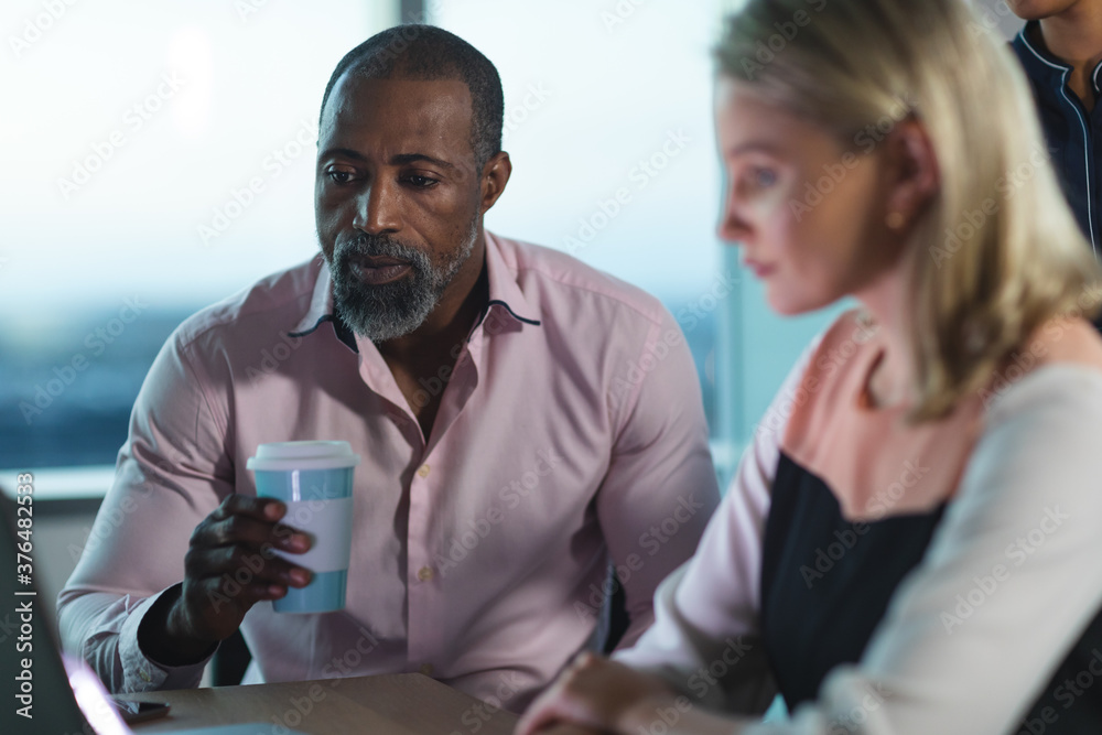 Senior Black African American businessman drinking coffee while young businesswoman using laptop at modern office Senior Black African American businessman drinking coffee while young businesswoman using laptop at modern office