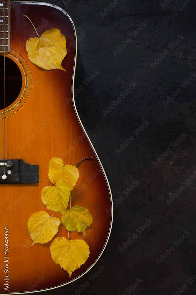 Fototapeta premium Acoustic guitar and yellow autumn leaves on dark brown background