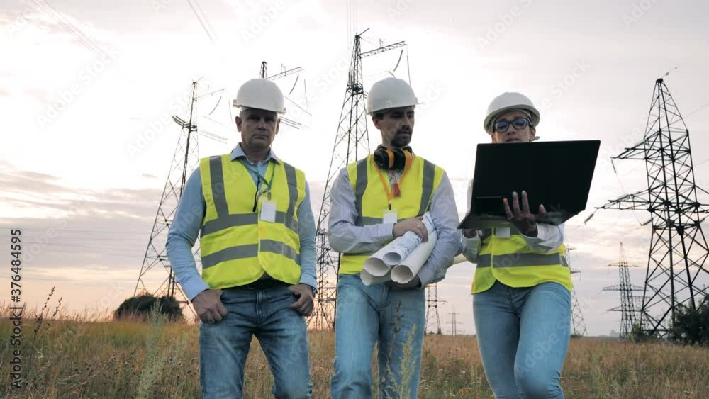 Energy workers walk in a field, working with laptop. Energy workers walk in a field, working with laptop.