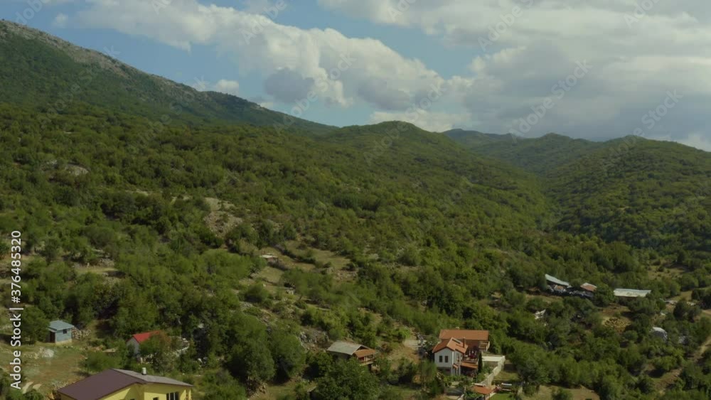 
Drone video of a village with houses and red roofs in the mountains with forest and peaks. Aerial shot Macedonia.