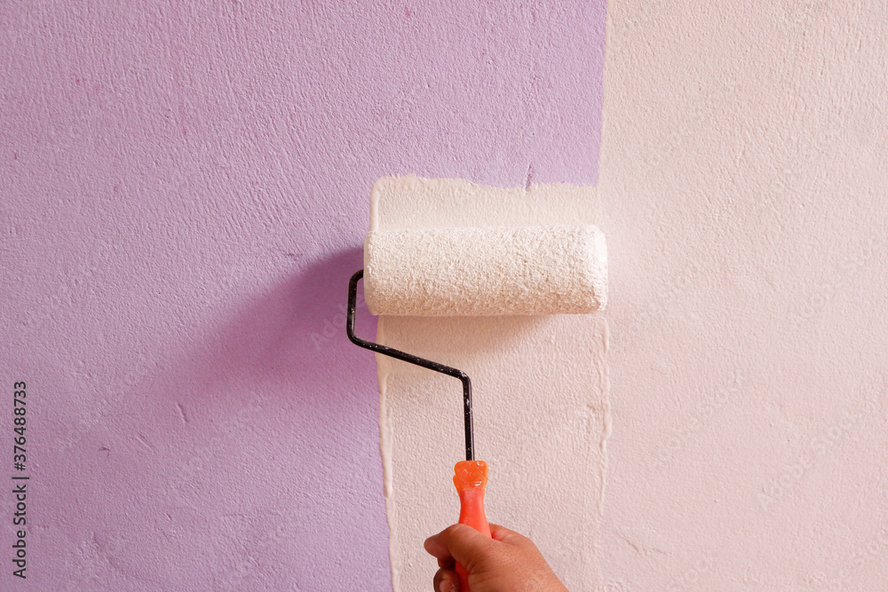 Obraz premium Hand holding a white paint roller on the wall