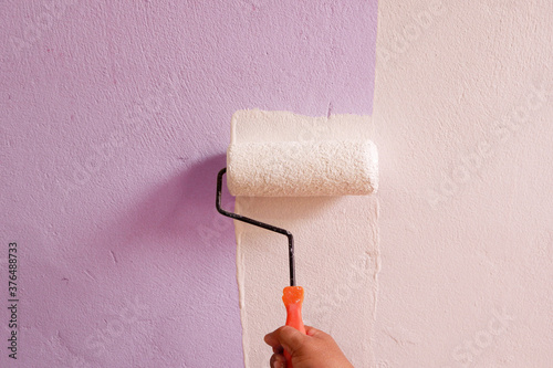 Hand holding a white paint roller on the wall