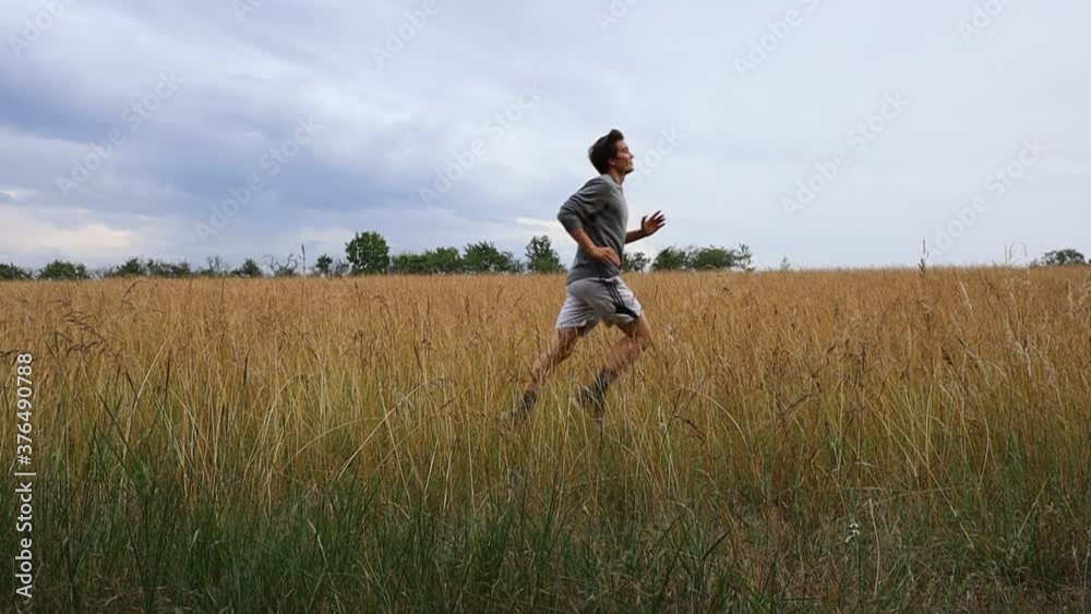 Slow Motion of Caucasian Young Man Running Through Field during Summer Cloudy Day. Slow Motion of Caucasian Young Man Running Through Field during Summer Cloudy Day.