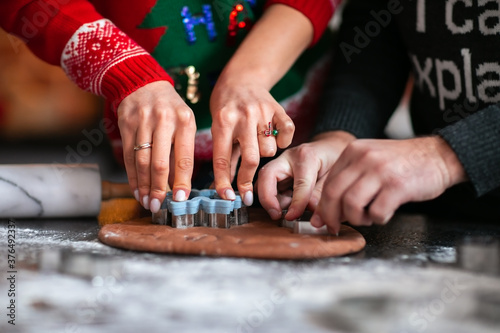 Man's and woman's hands in red and grey winter sweaters making cookies at the table.