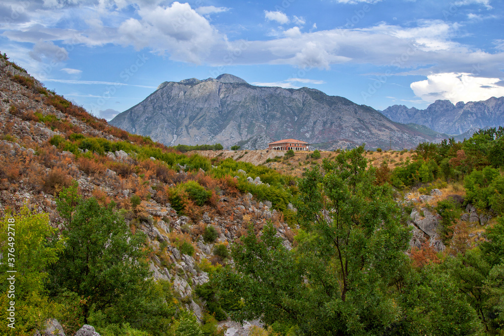 Naklejka premium View of canyon in Albanian mountains. Summer landscape with green trees, house on rocky hills and blue sky.