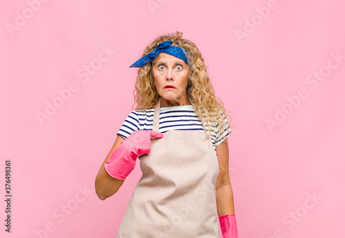 middle age womanfeeling confused, puzzled and insecure, pointing to self wondering and asking who, me? housekeeper concept photo