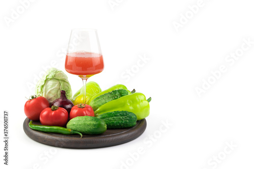 Fototapeta Naklejka Na Ścianę i Meble -  A glass of freshly squeezed vegetable juice and fresh vegetables on a round tray on a white background. Vegetable background. The concept of proper nutrition.
