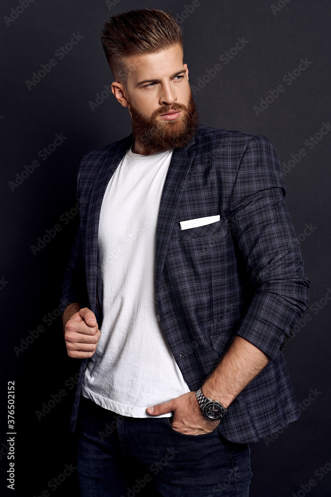 Handsome man with perfect hairdo and beard looking away while standing against black background Handsome man with perfect hairdo and beard looking away while standing against black background