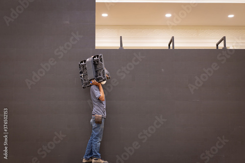 The young construction worker is assembling a large LED screen that will be used at the upcoming event.
