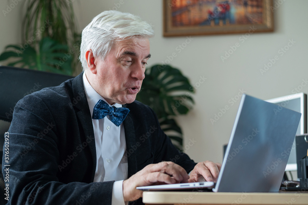 Mature gray-haired business man works at a laptop in the office. Mature gray-haired business man works at a laptop in the office.