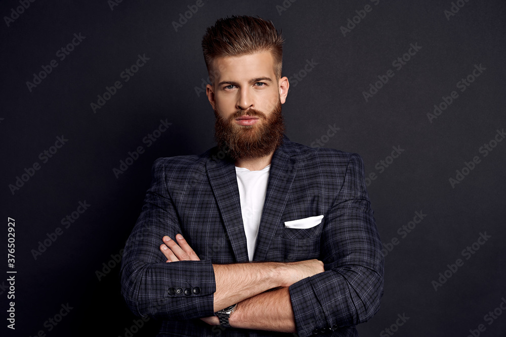 Handsome man keeping arms crossed and looking at camera while standing against grey background