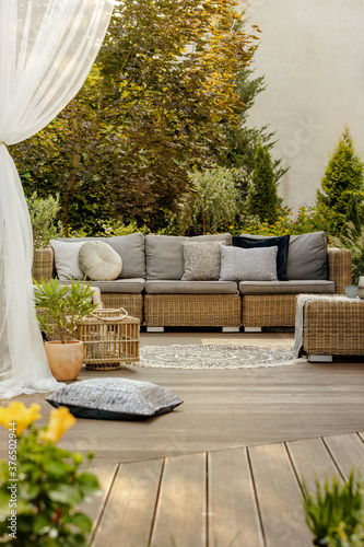 Comfortable wicker garden furniture with grey pillows in beautiful backyard