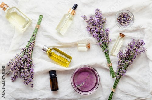 Set lavender oils serum and lavender flowers on white fabric. Skincare cosmetics products. Natural spa beauty products. Lavender essential oil, serum, body butter, massage oil, liquid. Flat lay